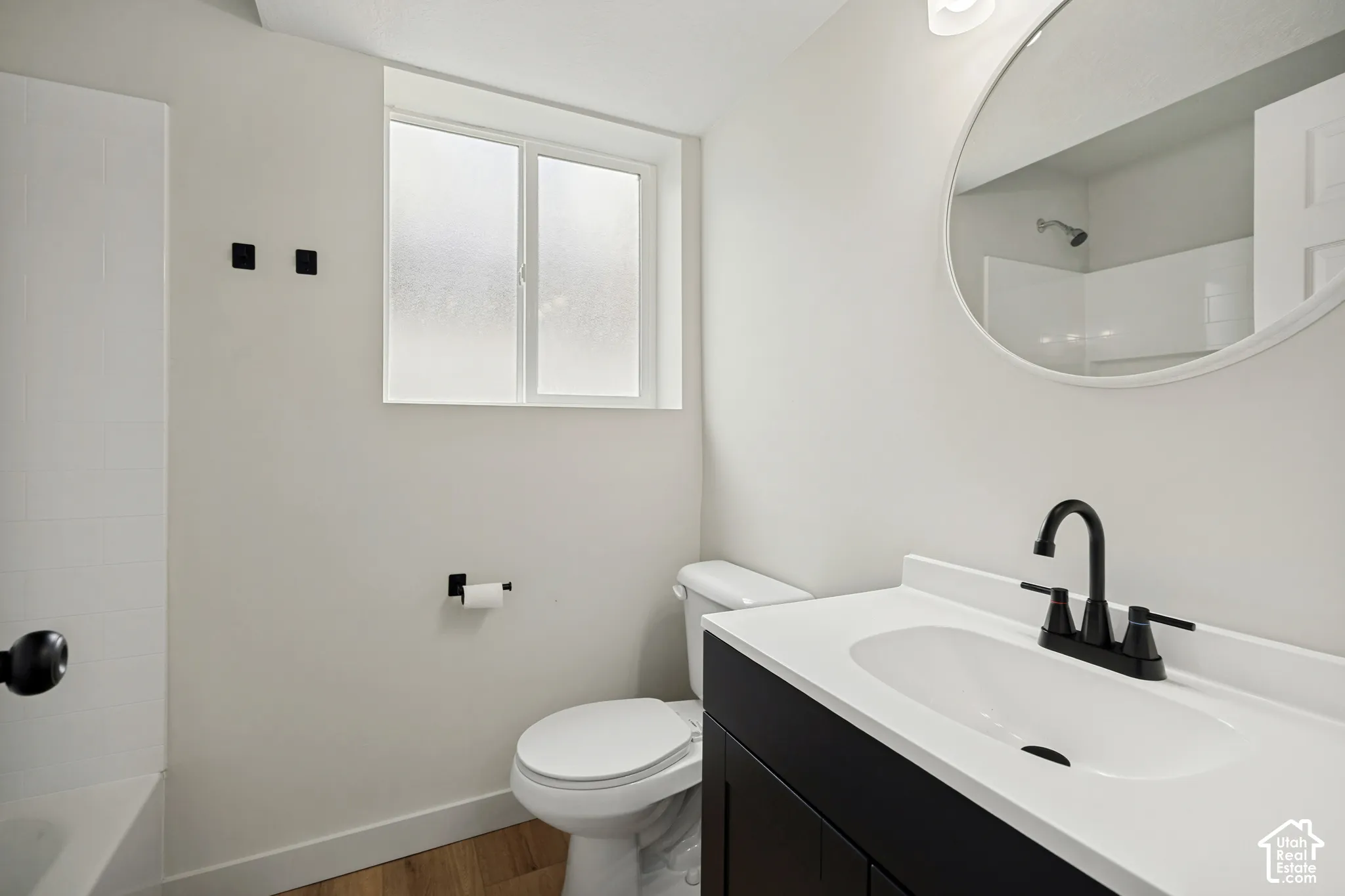Bathroom featuring a black vanity with a white countertop, round mirror, matte black faucet, and wood-finish flooring
