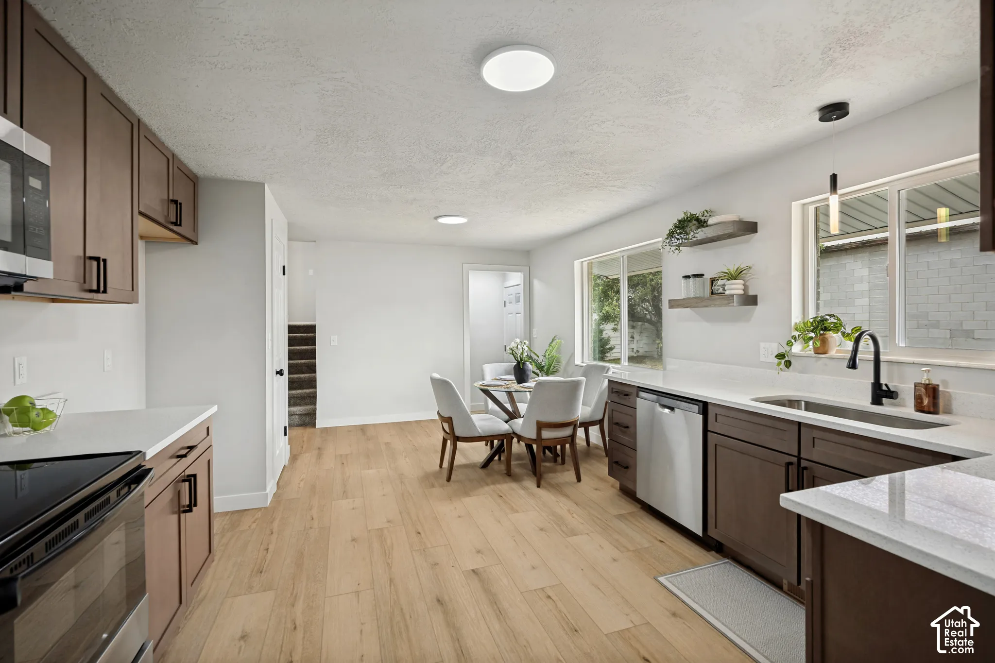 Modern kitchen featuring wood-finish flooring, white countertops, dark wood cabinetry, and stainless steel appliances