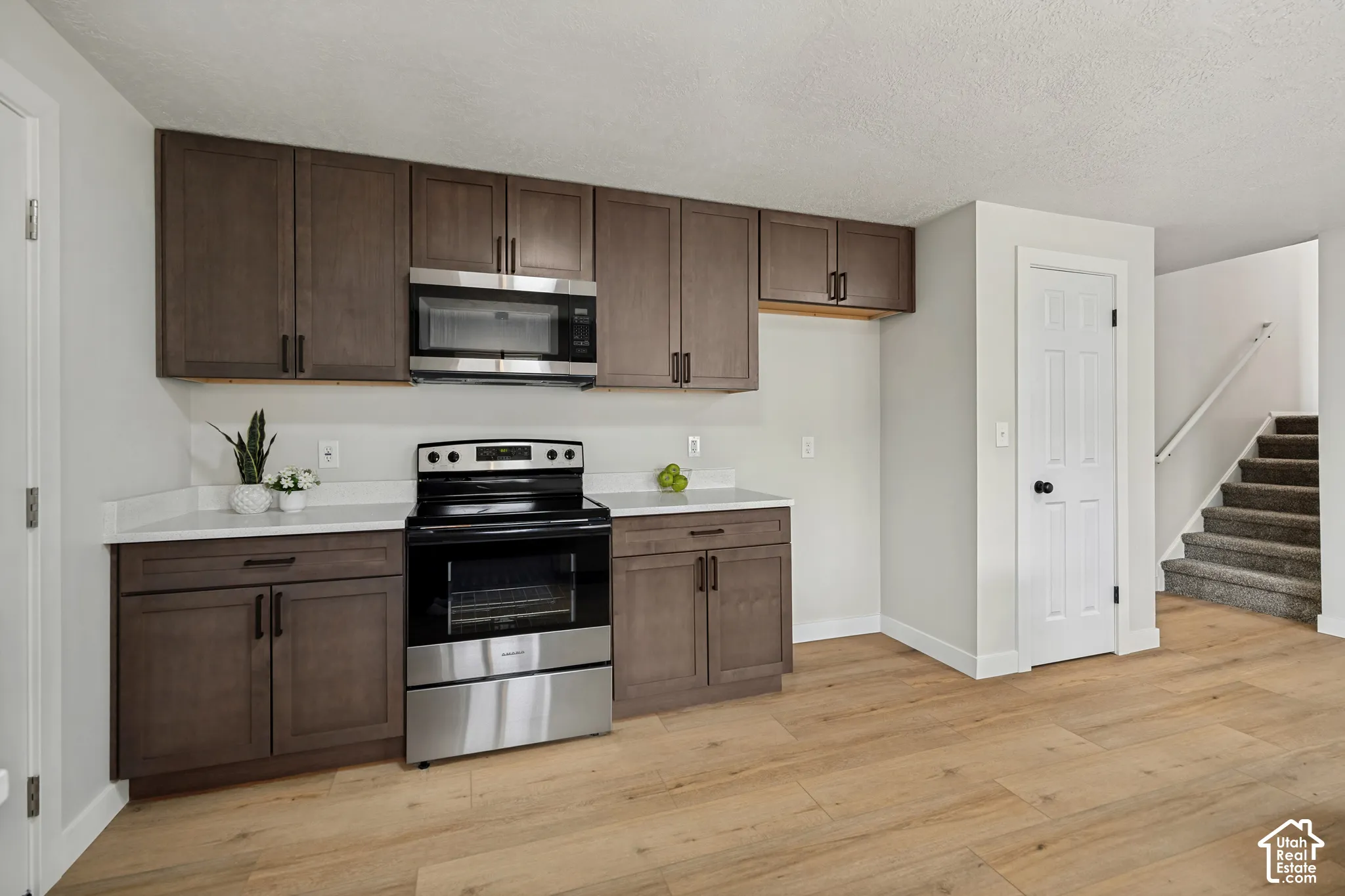 Modern kitchen featuring wood-finish flooring, white countertops, dark wood-finish cabinetry, and stainless steel appliances