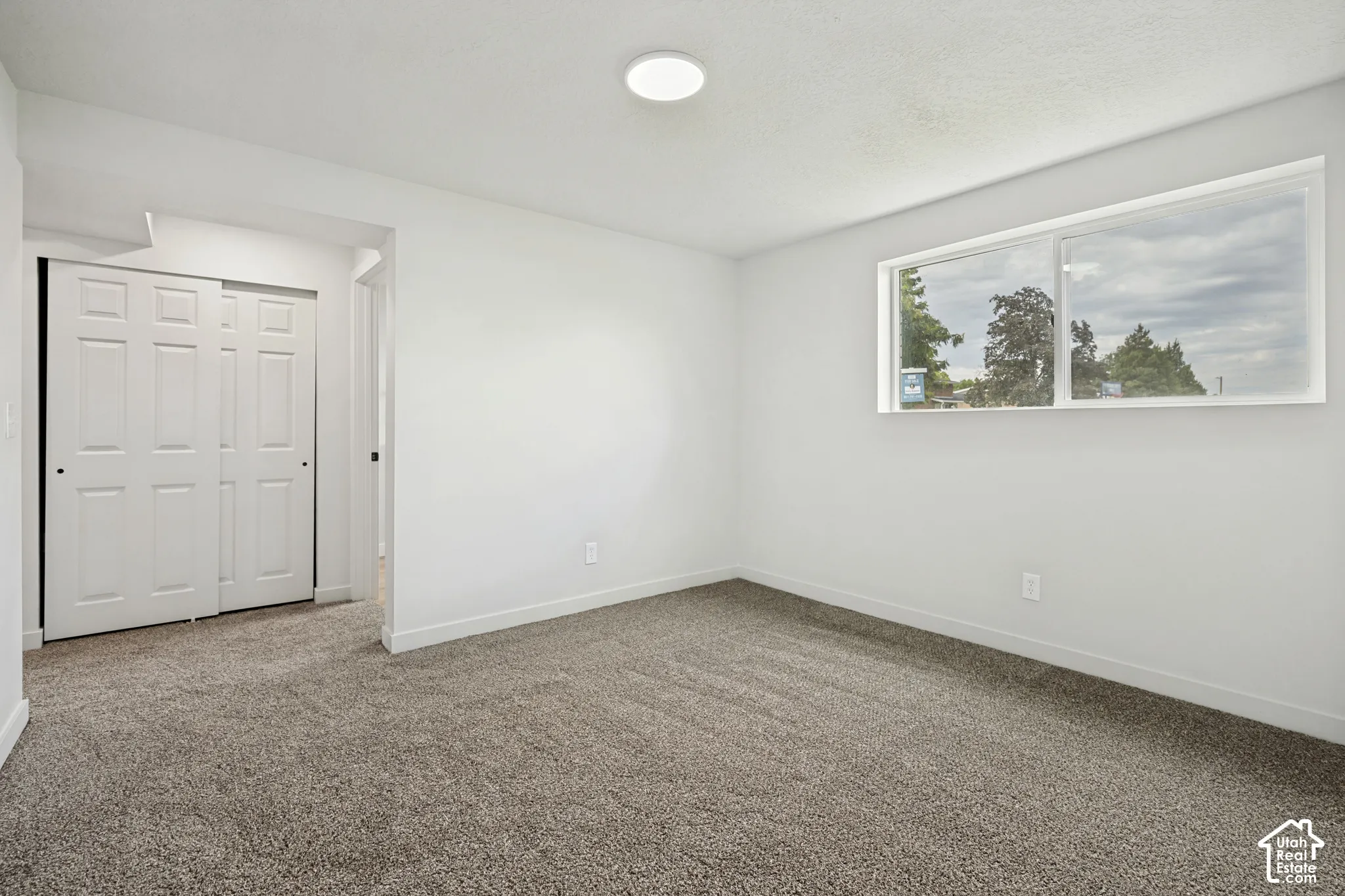 Recessed ceiling light fixture, neutral wall paint, gray carpeting, horizontal window, and bi-fold closet doors