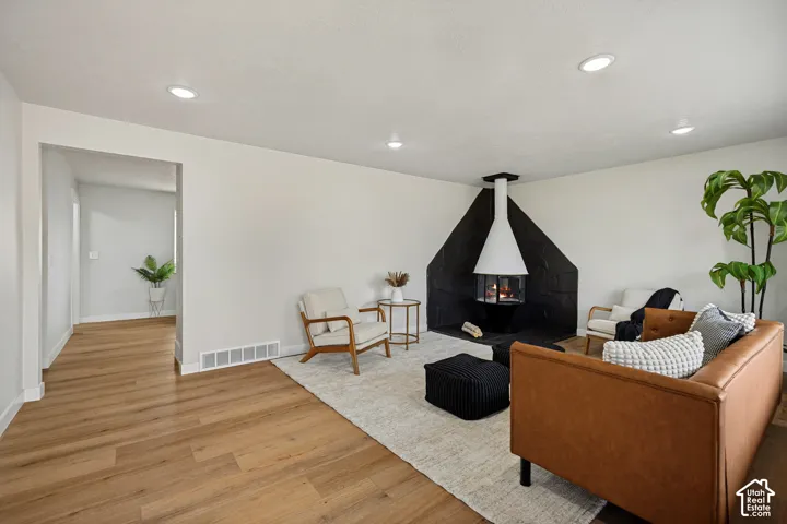 Recessed ceiling lighting, wood-finish flooring, and a black stone fireplace with a suspended white hood