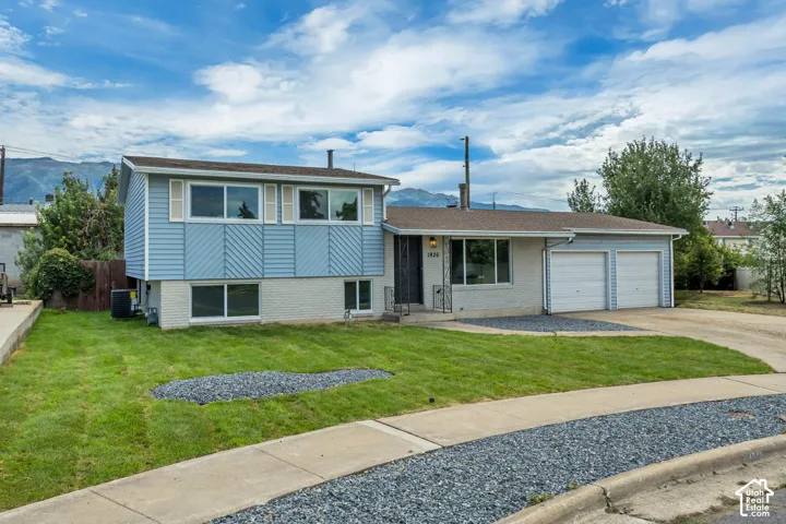 Split-level residence featuring blue siding and white brick, a two-car garage, and a manicured lawn