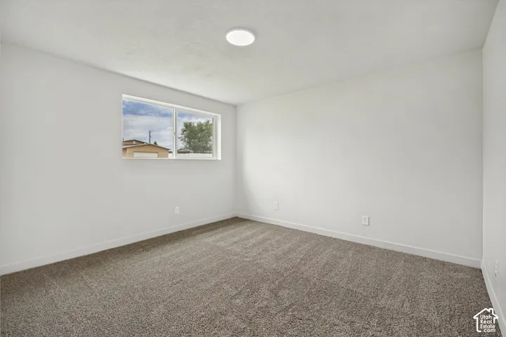 Light gray carpet flooring, white painted walls, single window, and a recessed ceiling light fixture