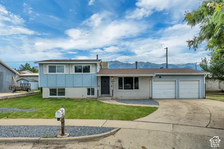 Split-level residence featuring a two-car attached garage, light blue siding, and white window shutters