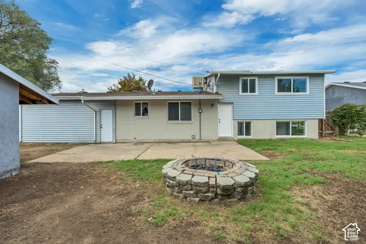 Rear exterior featuring a stone-clad fire pit, concrete patio, and a two-story addition with blue siding