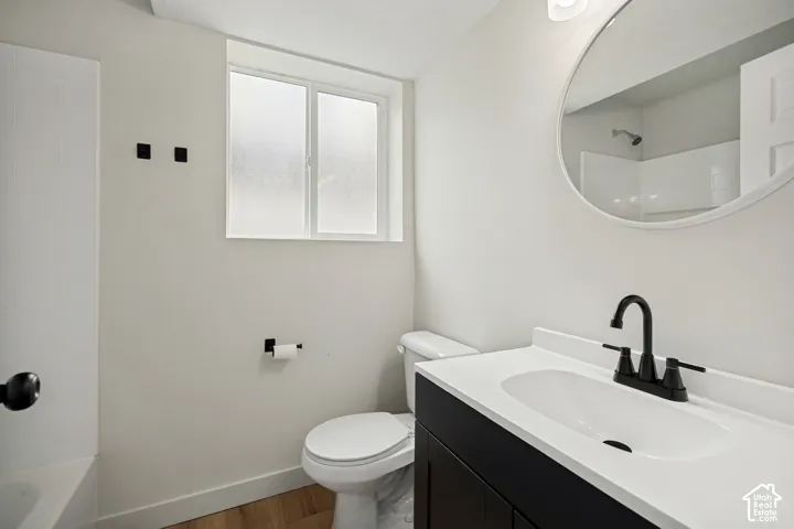 Bathroom featuring a black vanity with a white countertop, round mirror, matte black faucet, and wood-finish flooring