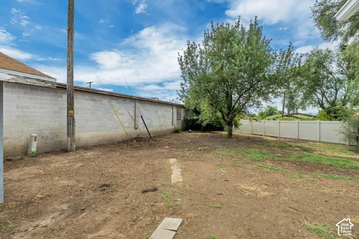 Expansive outdoor area featuring a mature tree, partial block wall, and white privacy fencing