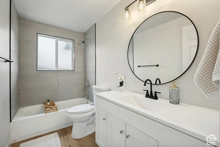 White vanity with integrated sink and matte black faucet, round mirror, and wood-finish flooring
