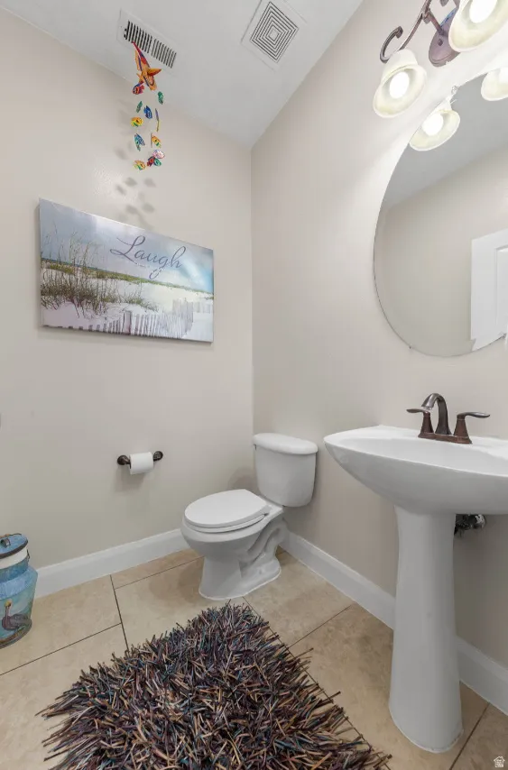 Pedestal sink with a bronze-finish faucet, white toilet, ceiling-mounted light fixture, and tile flooring