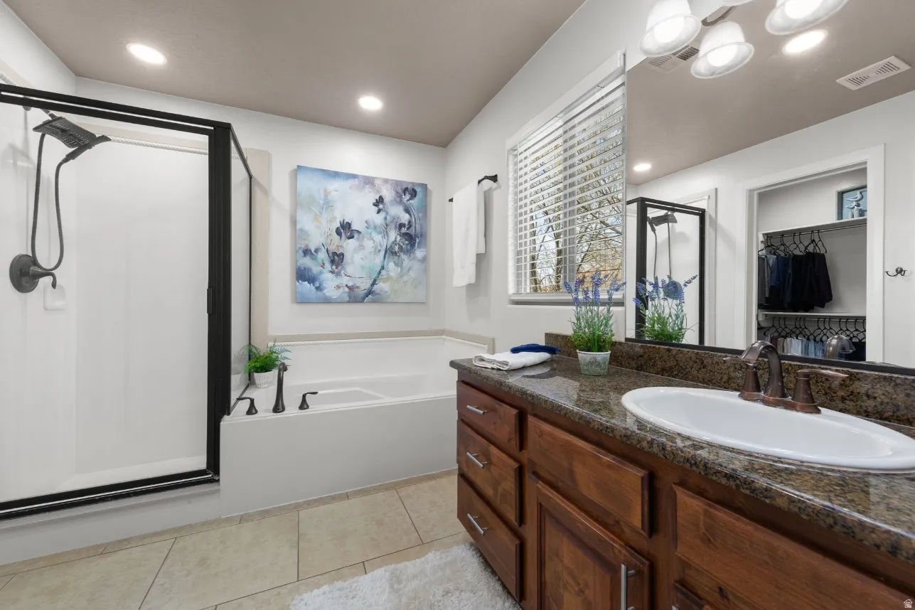 Recessed lighting, tiled flooring, wood-finish vanity with an undermount sink, built-in bathtub, and a glass-enclosed shower