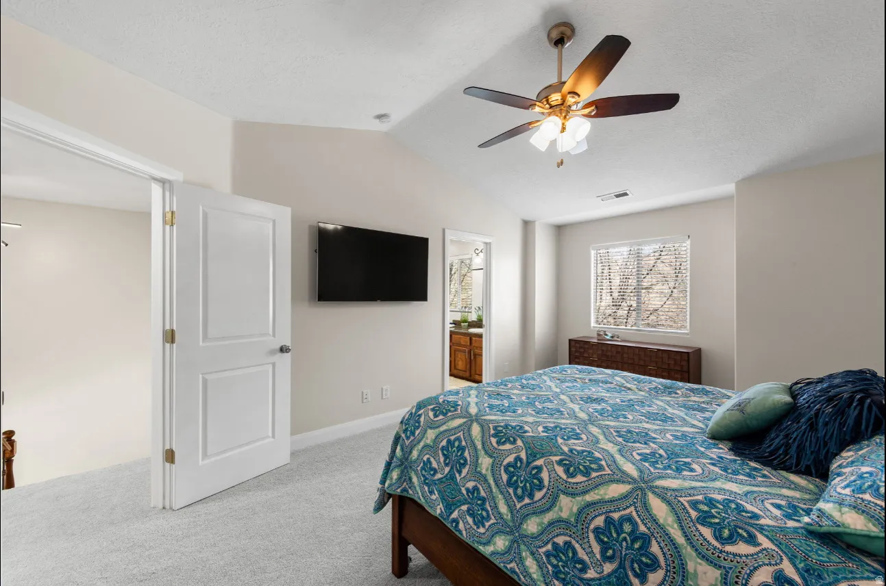 Vaulted ceiling bedroom with a ceiling fan with integrated lighting, soft neutral wall paint, and light-colored carpet