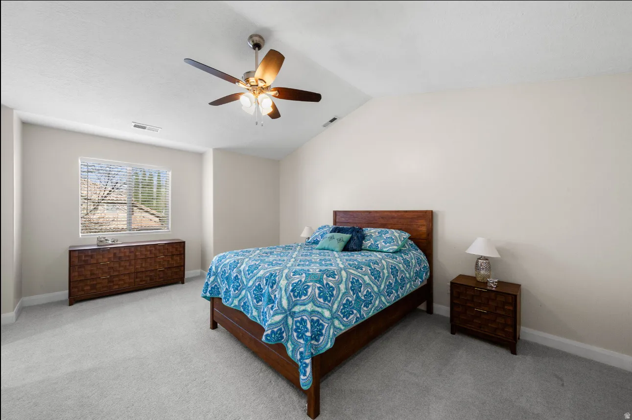 Vaulted ceiling with a ceiling fan, neutral wall paint, light gray carpet flooring, and a window with blinds