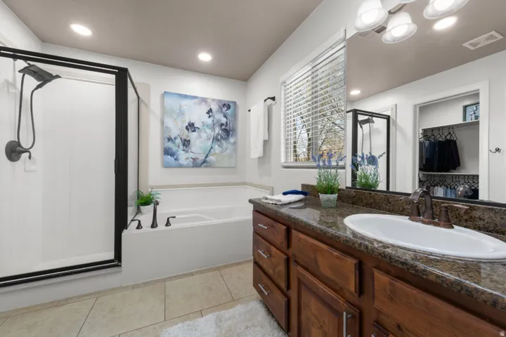 Recessed lighting, tiled flooring, wood-finish vanity with an undermount sink, built-in bathtub, and a glass-enclosed shower