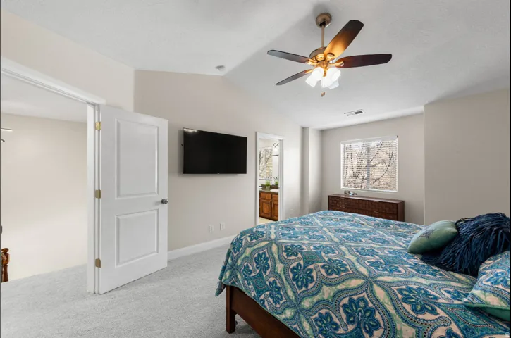 Vaulted ceiling bedroom with a ceiling fan with integrated lighting, soft neutral wall paint, and light-colored carpet