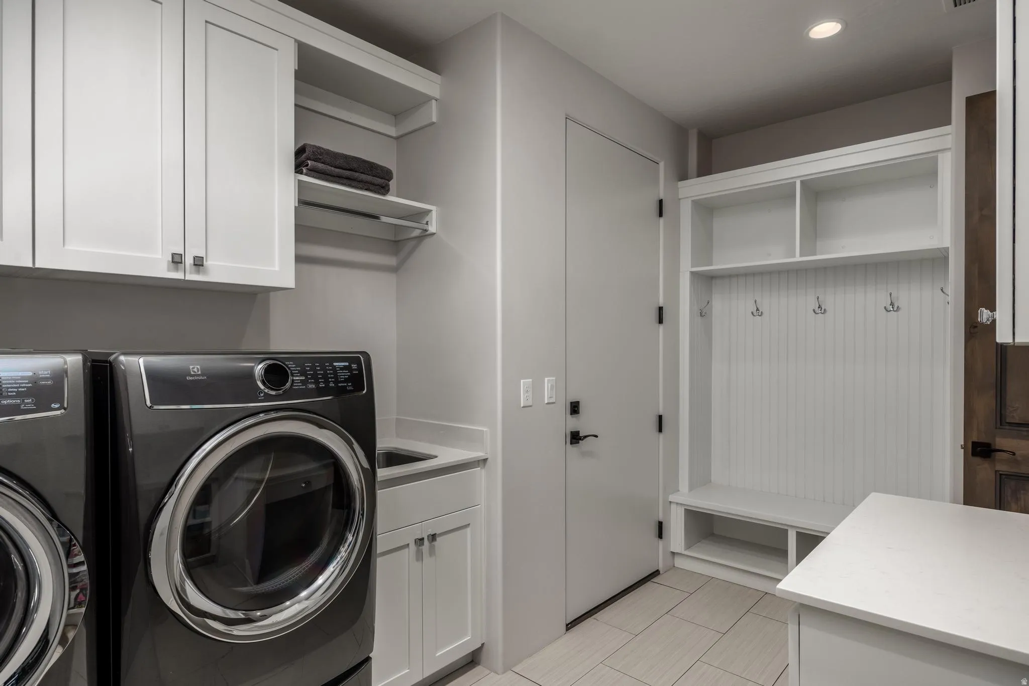 Dedicated laundry space featuring white shaker cabinetry, an integrated utility sink, and a built-in mudroom bench with storage