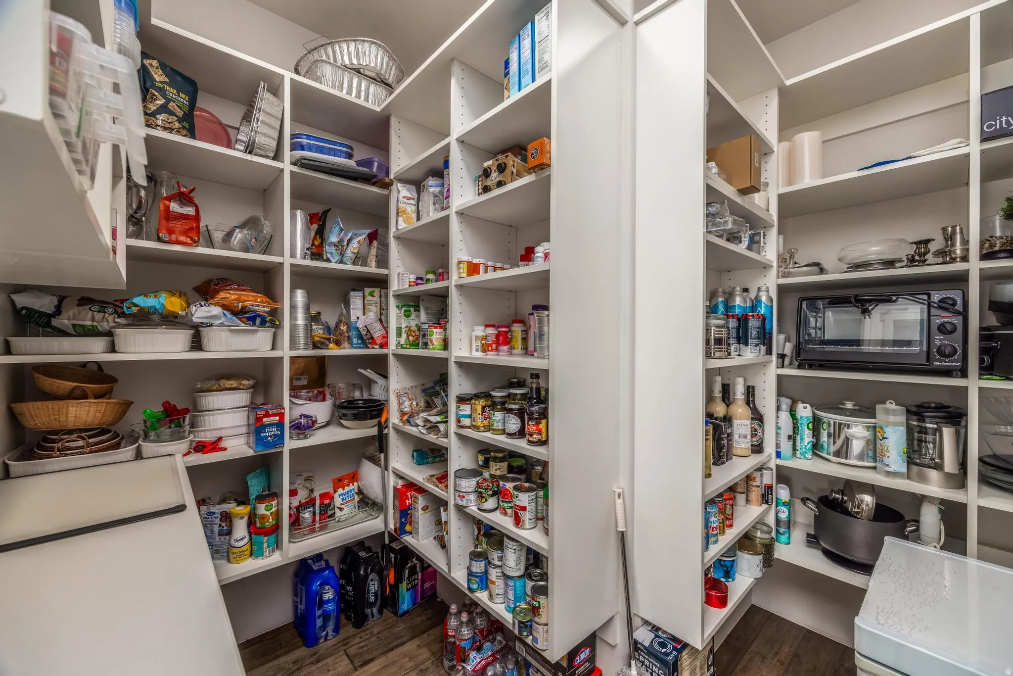 Spacious pantry with extensive built-in shelving, white finishes, and wood-finish flooring