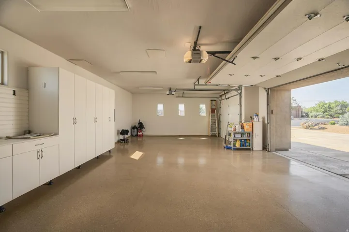 Spacious garage with multiple overhead doors, built-in white cabinetry, concrete flooring, and multiple light fixtures