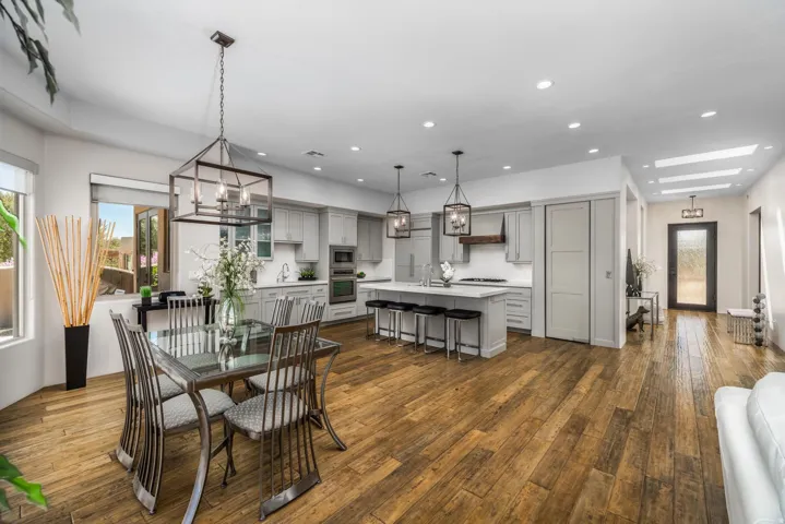 Wood-finish flooring throughout, kitchen with light cabinetry and white countertops, central island with seating, built-in oven, and recessed lighting