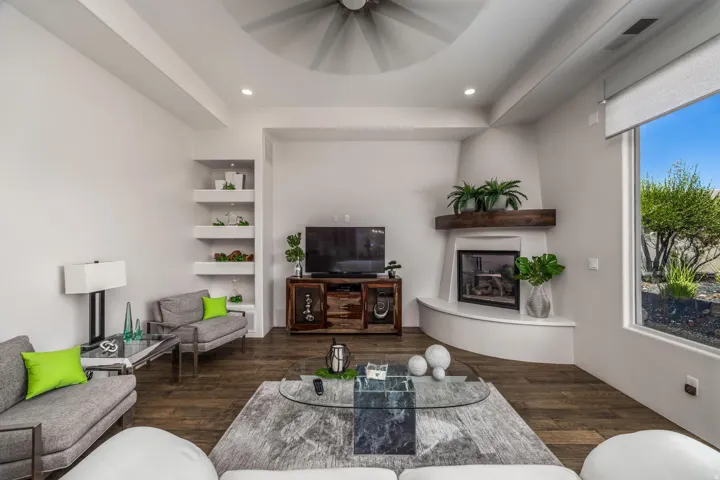 Wood-finish flooring, recessed lighting, built-in shelving, corner fireplace with wood mantel, and a large window with roller shades