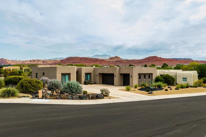 Desert modern exterior with a neutral stucco finish, multiple garage entrances, and a curved paved driveway