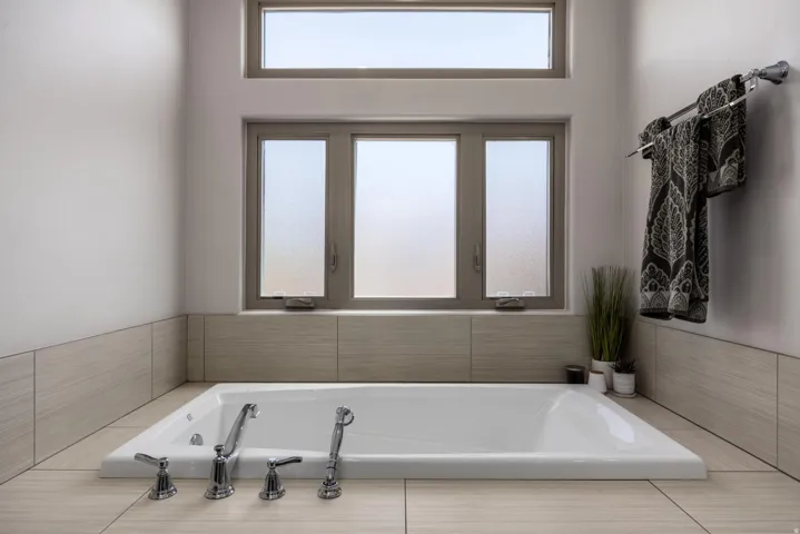 Primary Bathroom. Built-in soaking tub with polished chrome fixtures, surrounded by large format tile