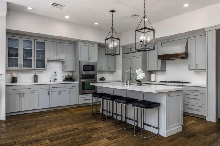 Modern kitchen featuring light gray cabinetry, stainless steel appliances, a white subway tile backsplash, a central island with countertop seating, and wood-finish flooring