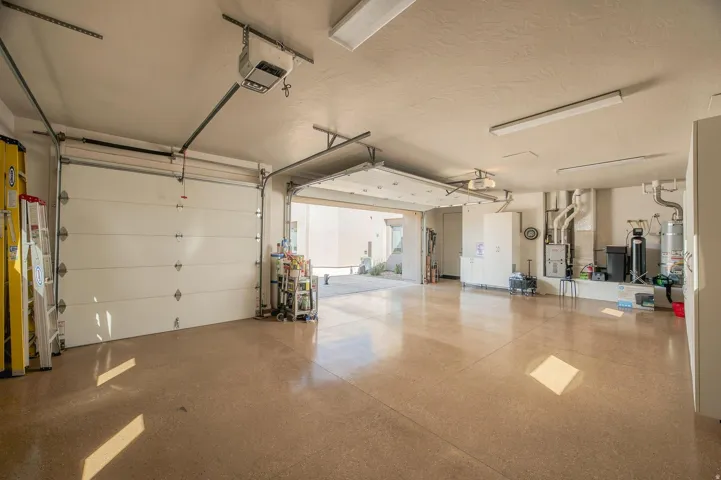 Spacious multi-bay garage with epoxy-coated flooring, multiple overhead fluorescent light fixtures, and a utility area featuring a water heater