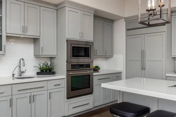 Light gray shaker cabinetry with brushed nickel hardware, stainless steel built-in appliances, white subway tile backsplash, white countertop surfaces, and a built-in refrigerator