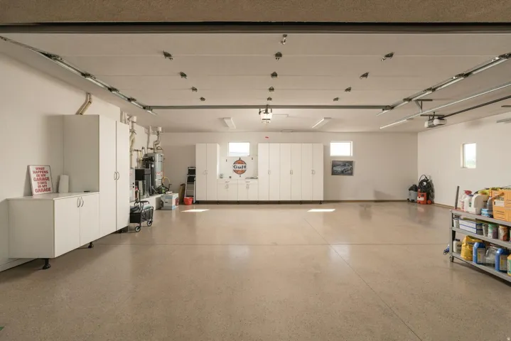 Spacious garage featuring a durable concrete floor, extensive built-in white cabinetry, multiple windows for natural light, and overhead fluorescent lighting