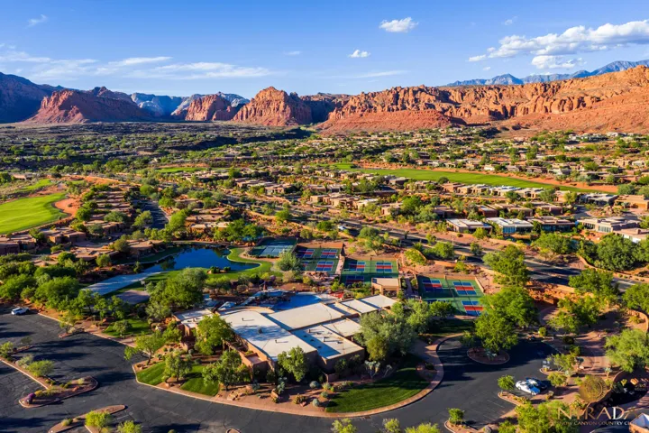 Community featuring multiple tennis courts, a central pond, surrounding residential structures, and a golf course, all set against a prominent red rock mountain backdrop