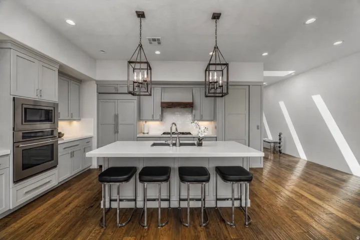 Kitchen featuring light gray cabinetry, stainless steel appliances, a center island with countertop seating, wood-finish flooring, and two pendant light fixtures