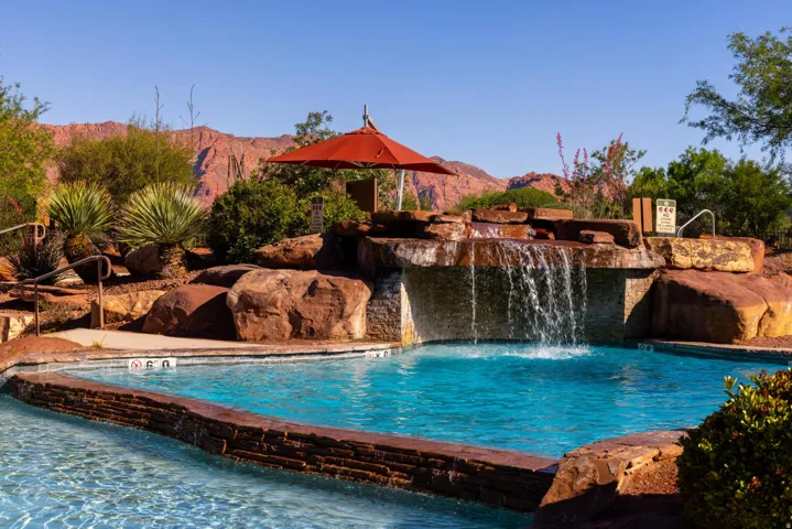 Swimming pool with a rock waterfall feature, integrated stone planters, and surrounding desert landscaping