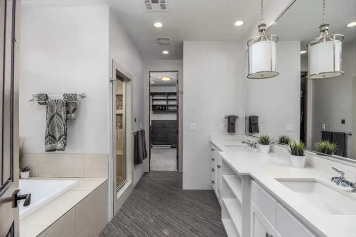 Dual vanity with white cabinetry and integrated sinks, full-width mirror, recessed lighting, and a built-in bathtub. Primary Bathroom