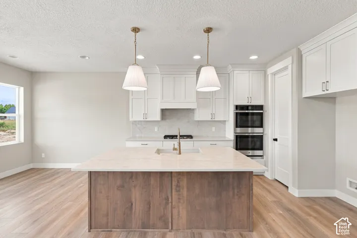 Kitchen featuring a wood-finish island with integrated sink, white cabinetry, stainless steel double ovens, and wood-finish flooring
