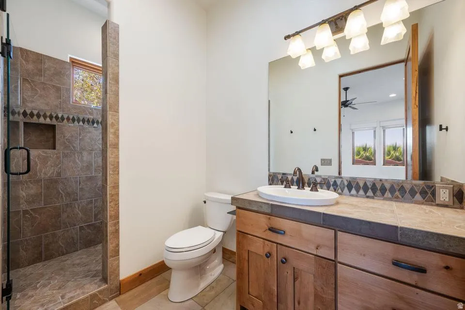 Walk-in shower with tiled surround and built-in niche, wood-finish vanity with an undermount sink, tiled countertop, and a large vanity mirror with overhead lighting