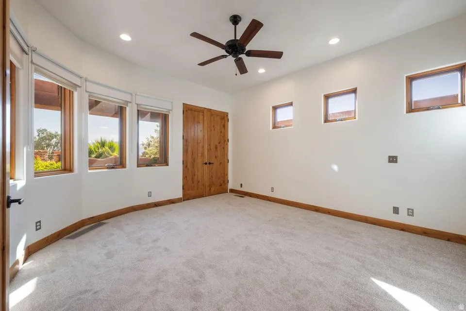 Plush carpet flooring, recessed lighting, wood-framed windows, wood double doors, and a ceiling fan