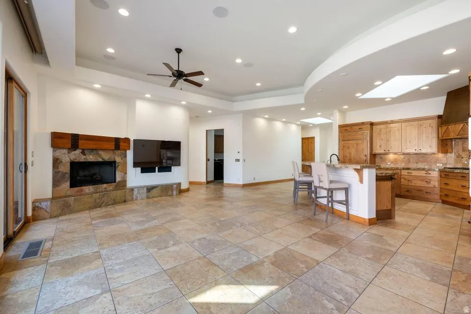 Spacious interior featuring large format tile flooring, a stone-clad fireplace, and a kitchen with wood cabinetry and a breakfast bar