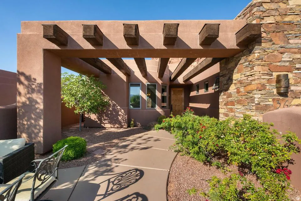 Architectural entry featuring a wood-beam pergola, stucco exterior, stacked stone accents, and a curved concrete pathway