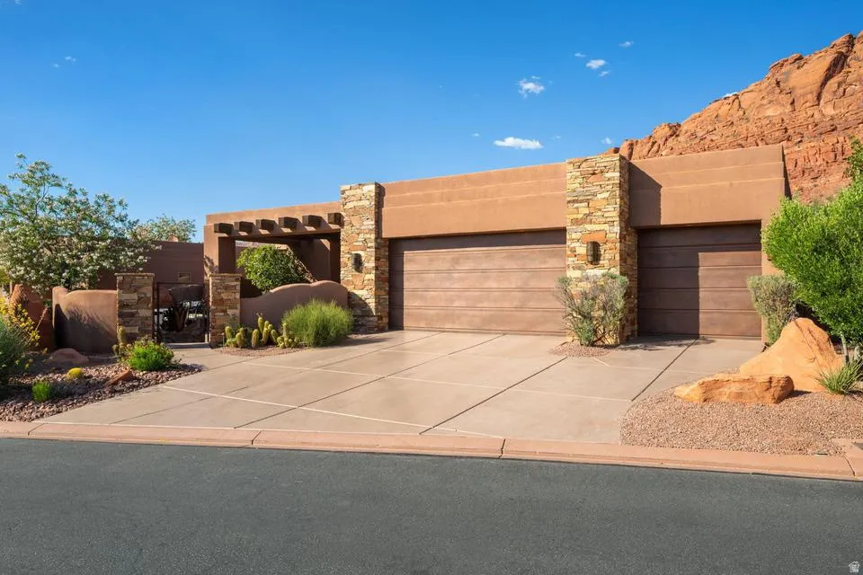 Stucco exterior with stone accents, two wood-finish garage doors, concrete driveway, and desert landscaping