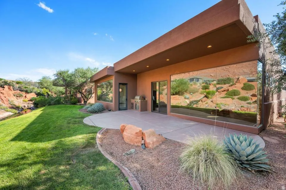 Expansive green lawn, hardscaping with gravel accents, built-in outdoor grill, large windows, and a paved patio area