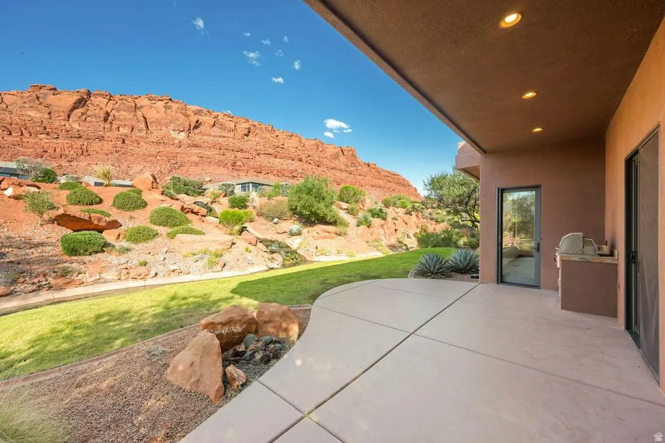 Expansive concrete patio with a built-in outdoor kitchen, recessed lighting, and direct access to a landscaped yard