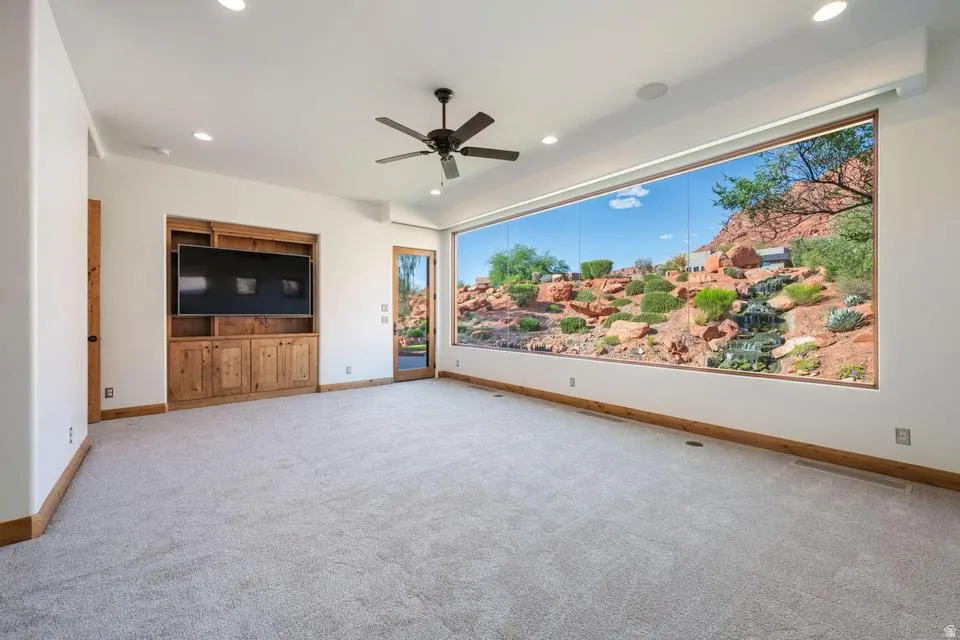 Expansive wall-to-wall window, recessed lighting, ceiling fan, carpeted flooring, and built-in wood cabinetry