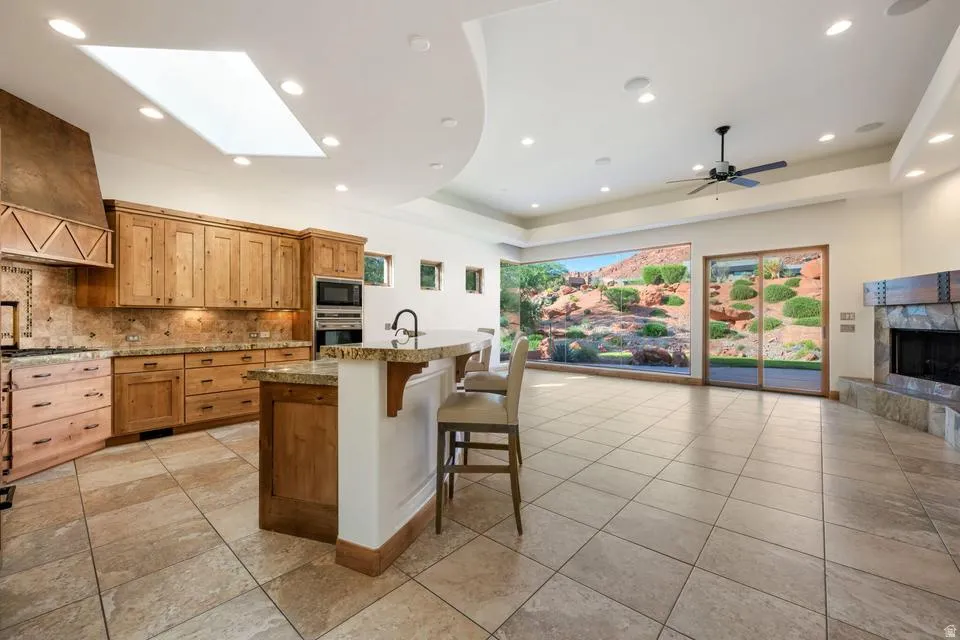 Extensive tile flooring, kitchen with wood cabinetry and stone countertops, built-in stainless steel double ovens, skylight, and a stone-clad fireplace
