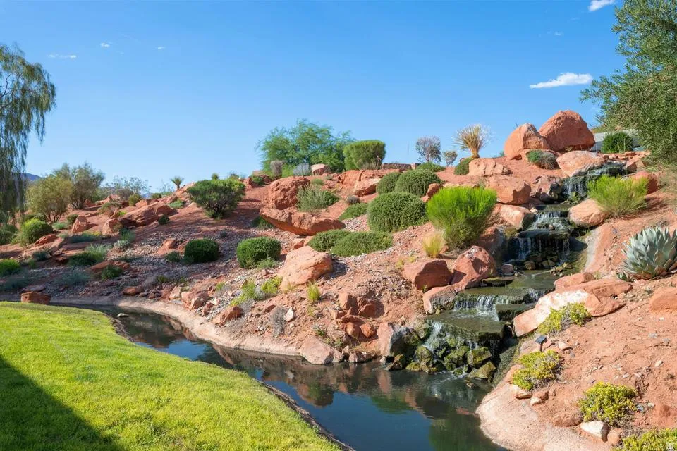 Expansive outdoor landscaping featuring a flowing water feature, manicured lawn, natural rock formations, and varied shrubbery