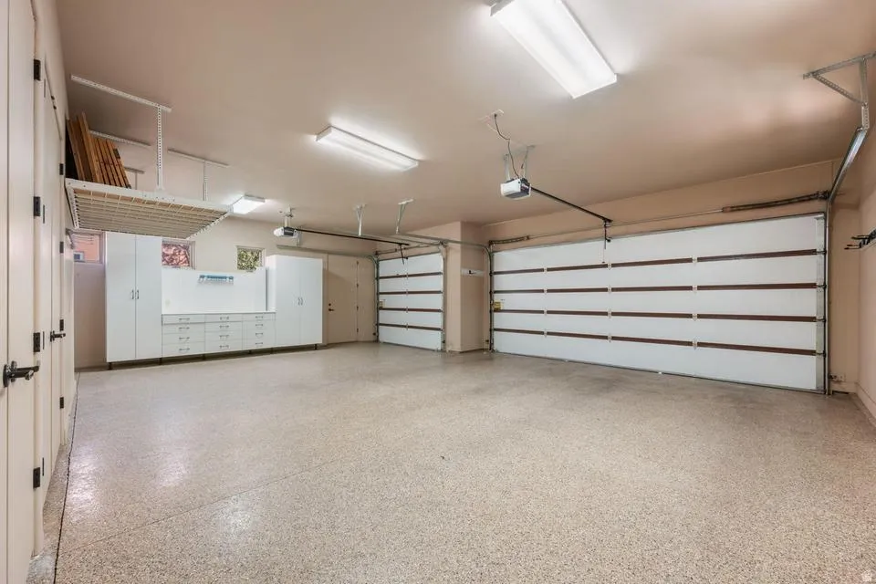 Spacious garage with two overhead doors, built-in cabinetry, overhead storage rack, and durable epoxy flooring