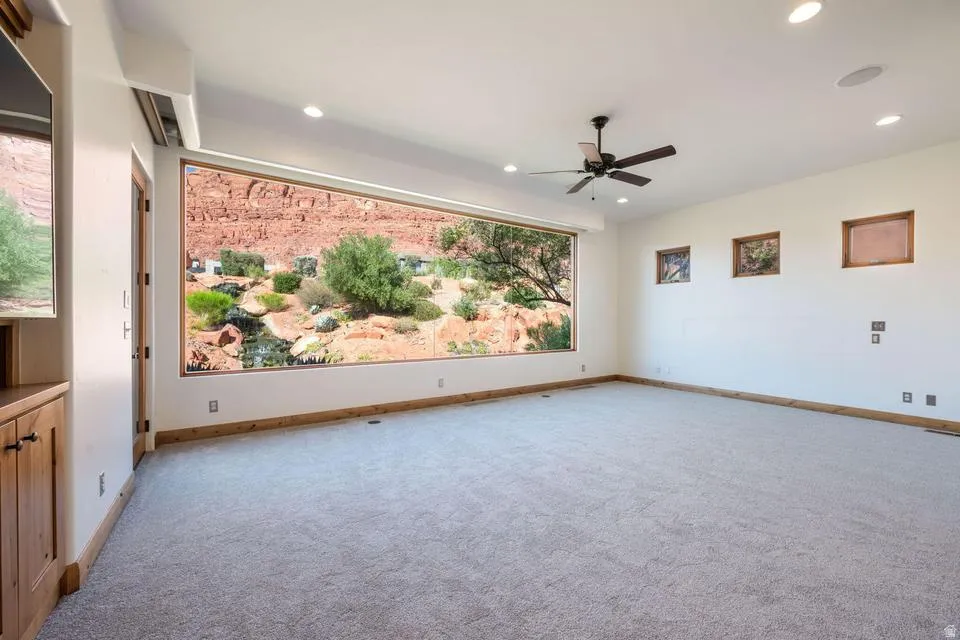 Expansive window offering a desert landscape, recessed lighting, ceiling fan, built-in cabinetry with wood-finish, and light-toned carpet