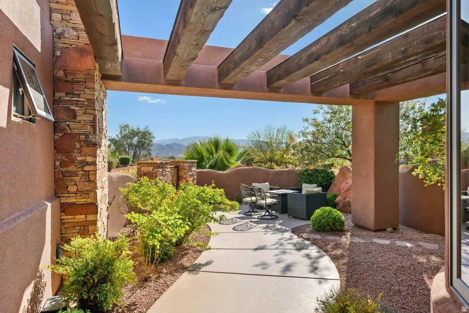 Covered patio with exposed wood beams, stone accent column, concrete pathway, and gravel landscaping