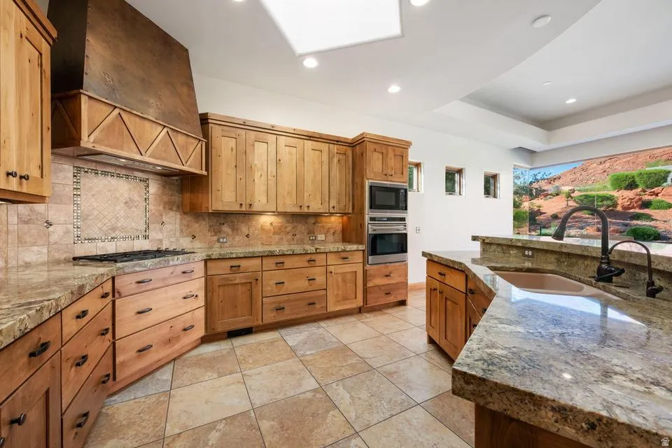 Wood cabinetry, stone countertops, tile flooring, built-in stainless steel appliances, and a skylight