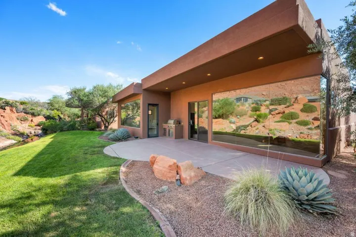 Expansive green lawn, hardscaping with gravel accents, built-in outdoor grill, large windows, and a paved patio area