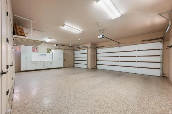 Spacious garage with two overhead doors, built-in cabinetry, overhead storage rack, and durable epoxy flooring